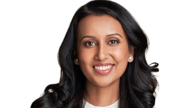 A woman with long, wavy black hair and brown skin smiles at the camera, radiating intentional health, wearing a light-colored top and stud earrings against a transparent background.