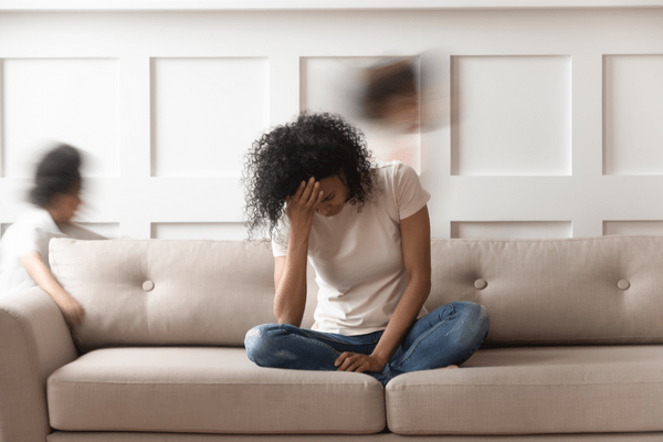 a tired woman suffering from a glutathione deficiency sitting on a couch