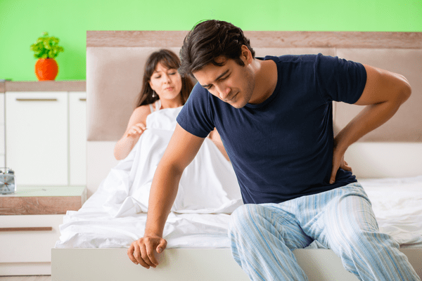 A man sitting at the end of a bed with an upset partner