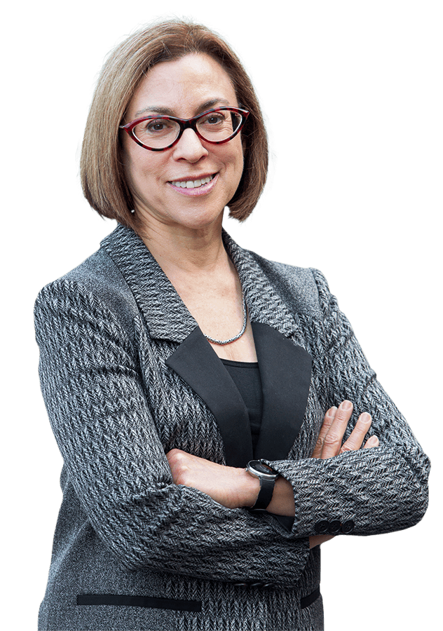 Dr. Gloria Mark, a woman with short brown hair and glasses, stands confidently with her arms crossed in a gray patterned blazer, smiling against a transparent background.