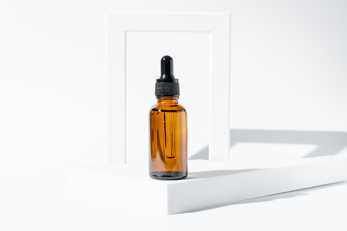 A brown glass dropper bottle with a black cap sits on a white geometric platform, set against a bright, minimal backdrop—an elegant way to buy Oral Semaglutide Drops for your wellness routine.