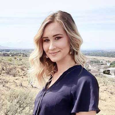 A woman with wavy blonde hair, wearing a navy blue top, stands outdoors with a dry, brushy landscape and distant houses—part of a peaceful scene often depicted in campaigns raising awareness about erectile dysfunction.
