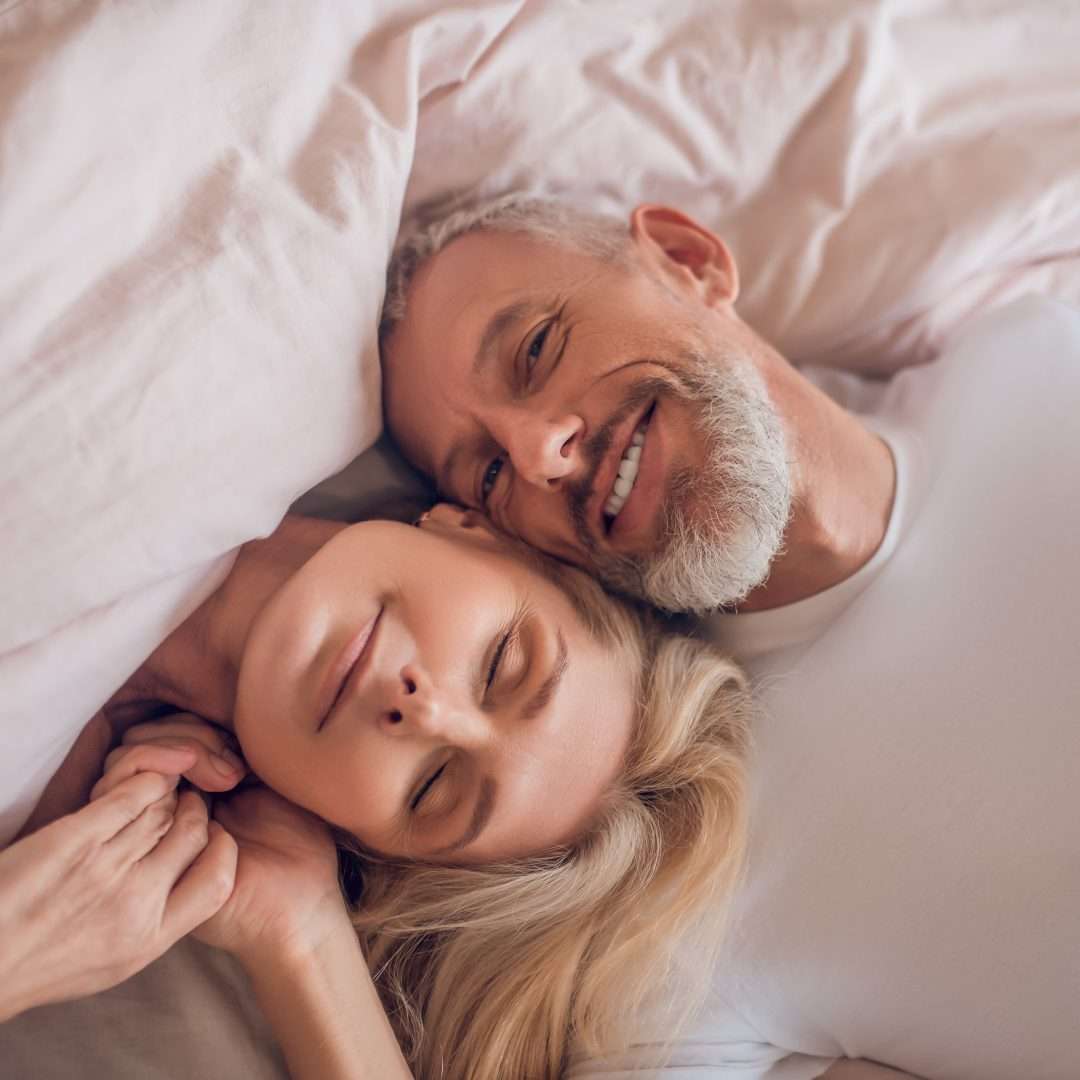 A couple laying in bed, heads touching