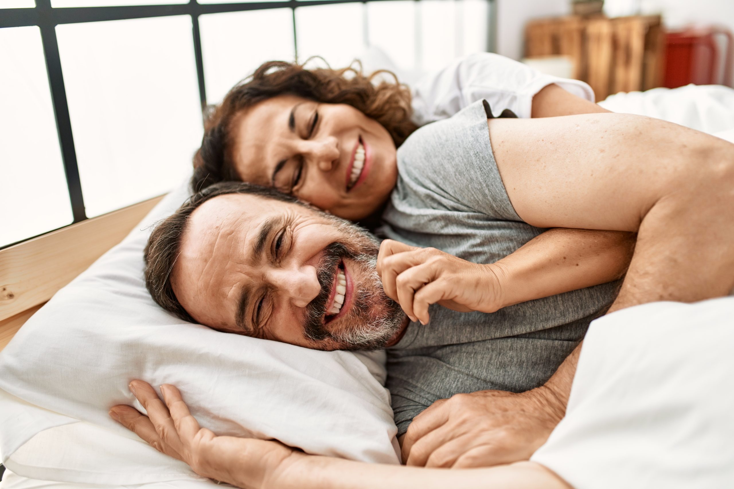 Middle Age Hispanic Couple Smiling Happy And Hugging Lying On A Bed
